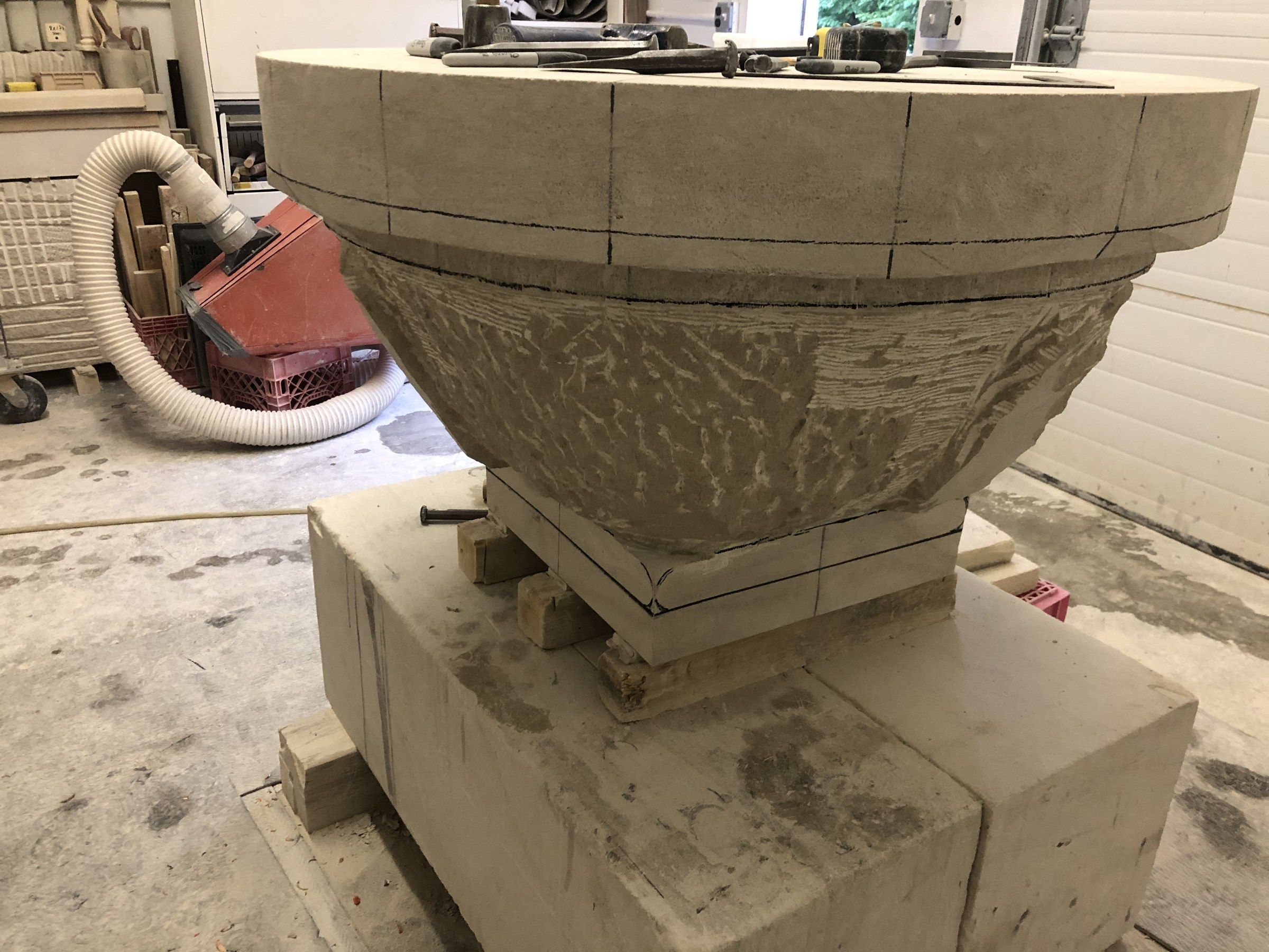 The round rim cut and marked in pencil, the body beneath still covered in point-chisel marks, resting on a square plinth with the foot drawn on it.