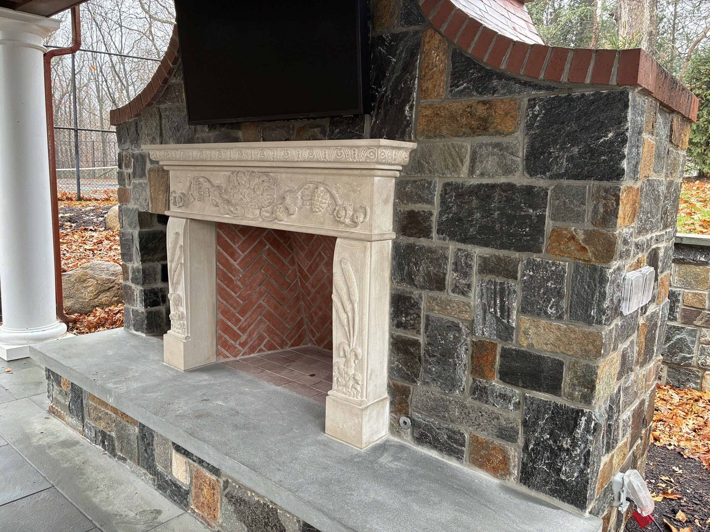 Three-quarter view from the left of the outdoor fireplace, with the carved limestone mantel set within the fieldstone wall.