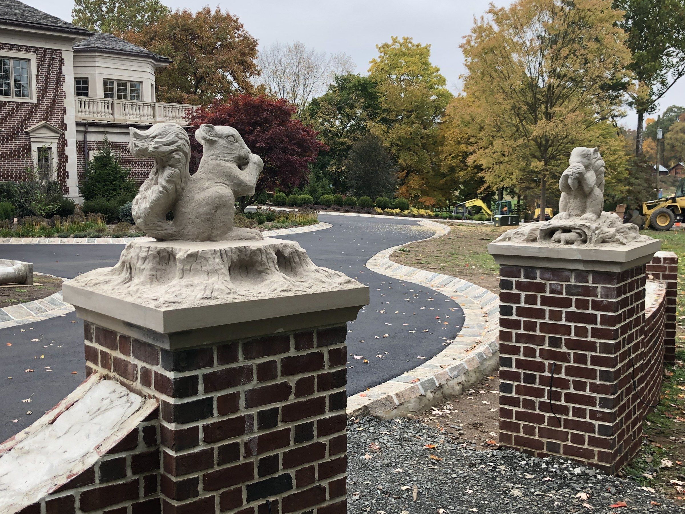 Both piers seen across the driveway entrance: a squirrel on a stump in the foreground, the second squirrel on the far pier.