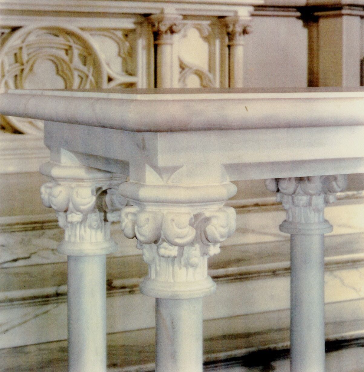 Close-up of one corner of the communion table: the molded marble top and apron resting on round colonnettes, each crowned by a capital of curling, deeply undercut foliage.