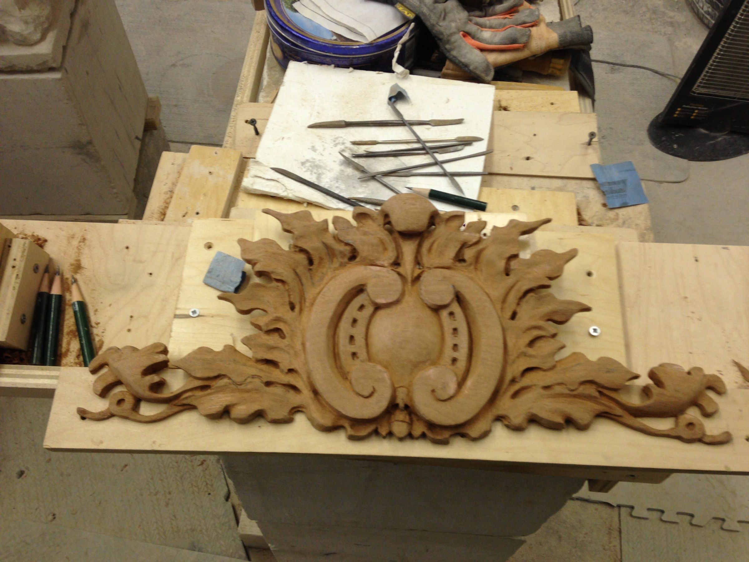 The finished cartouche laid on a board on the workbench, with rasps and pencils nearby.