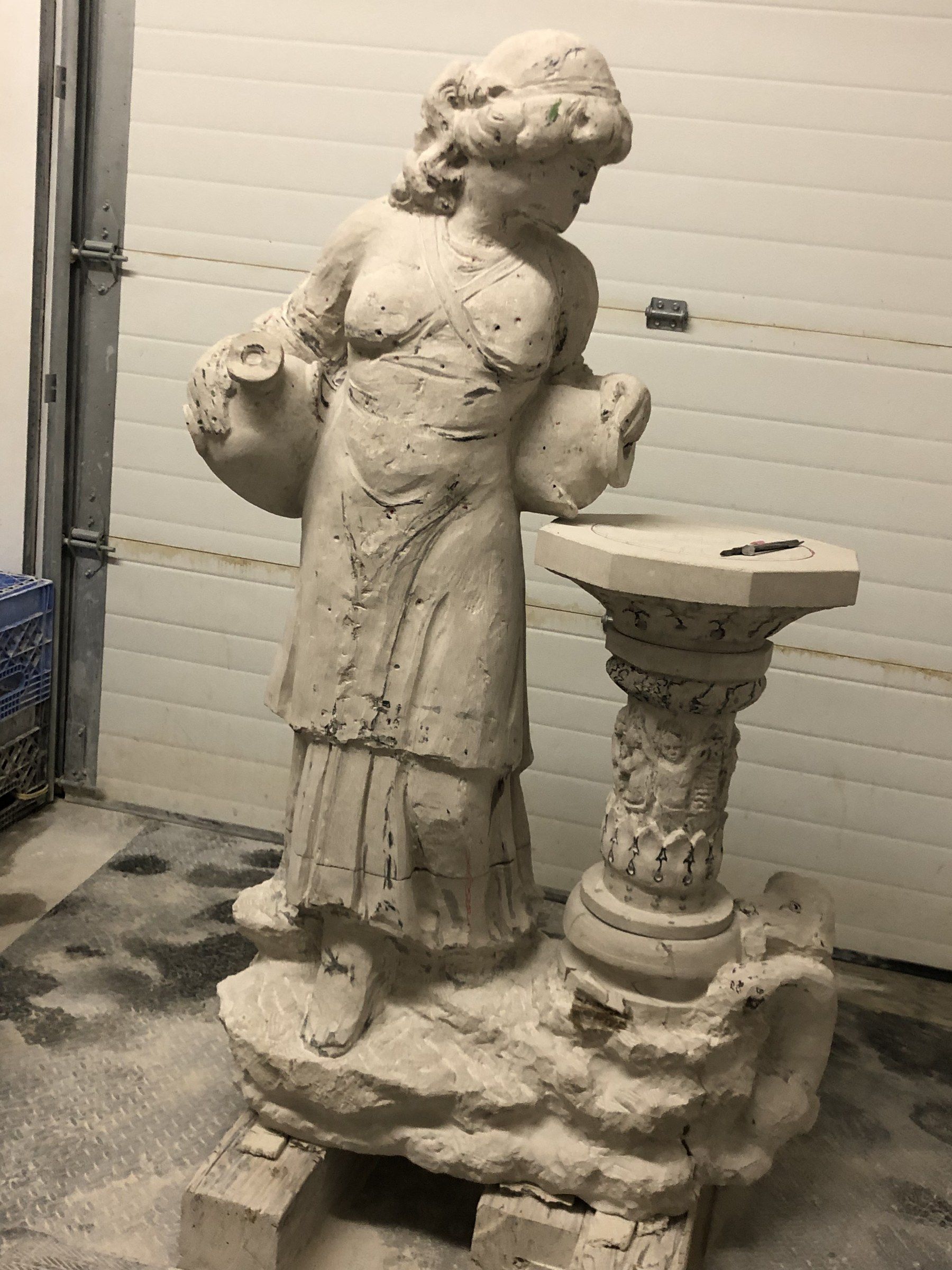 The figure and column in progress, still marked with pencil lines, on a rough rocky base set on wooden blocks.