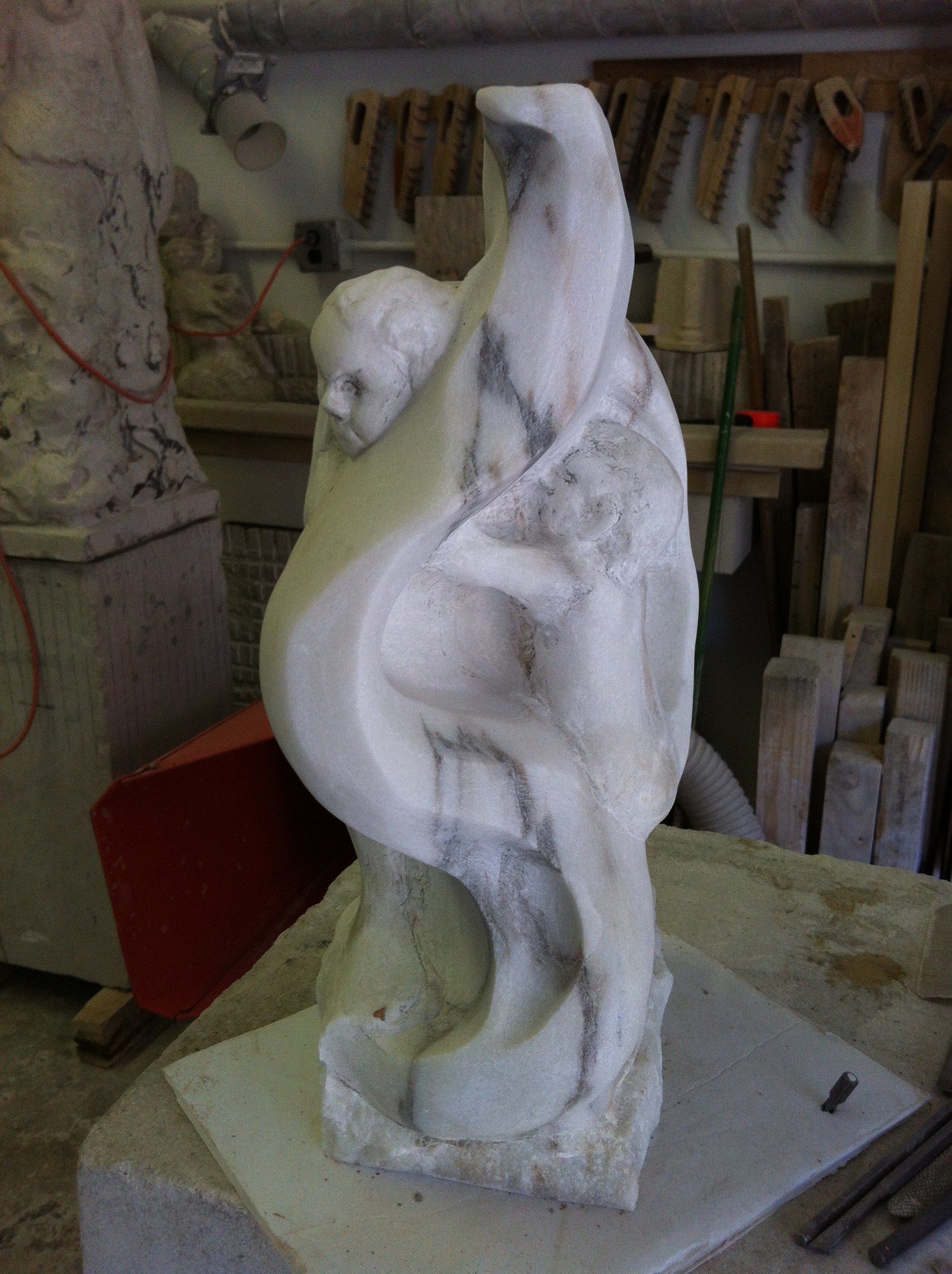 La sculpture vue de côté : la tête de l'enfant et la grande courbe du marbre, ses veines grises parcourant la forme.