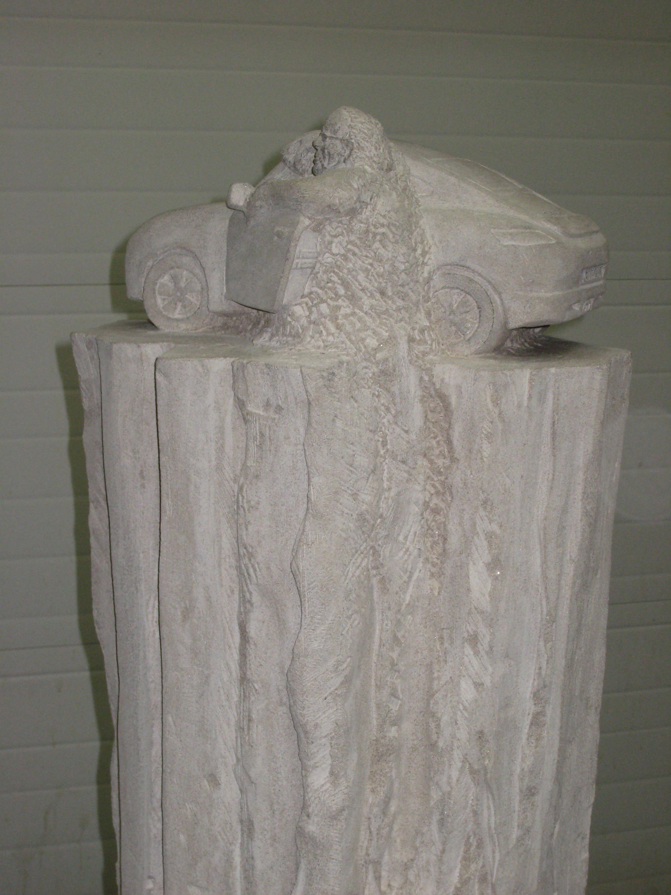 Détail de la voiture en pierre avec une figure taillée émergeant du corps du véhicule, sculptée à la main dans le même bloc de calcaire.