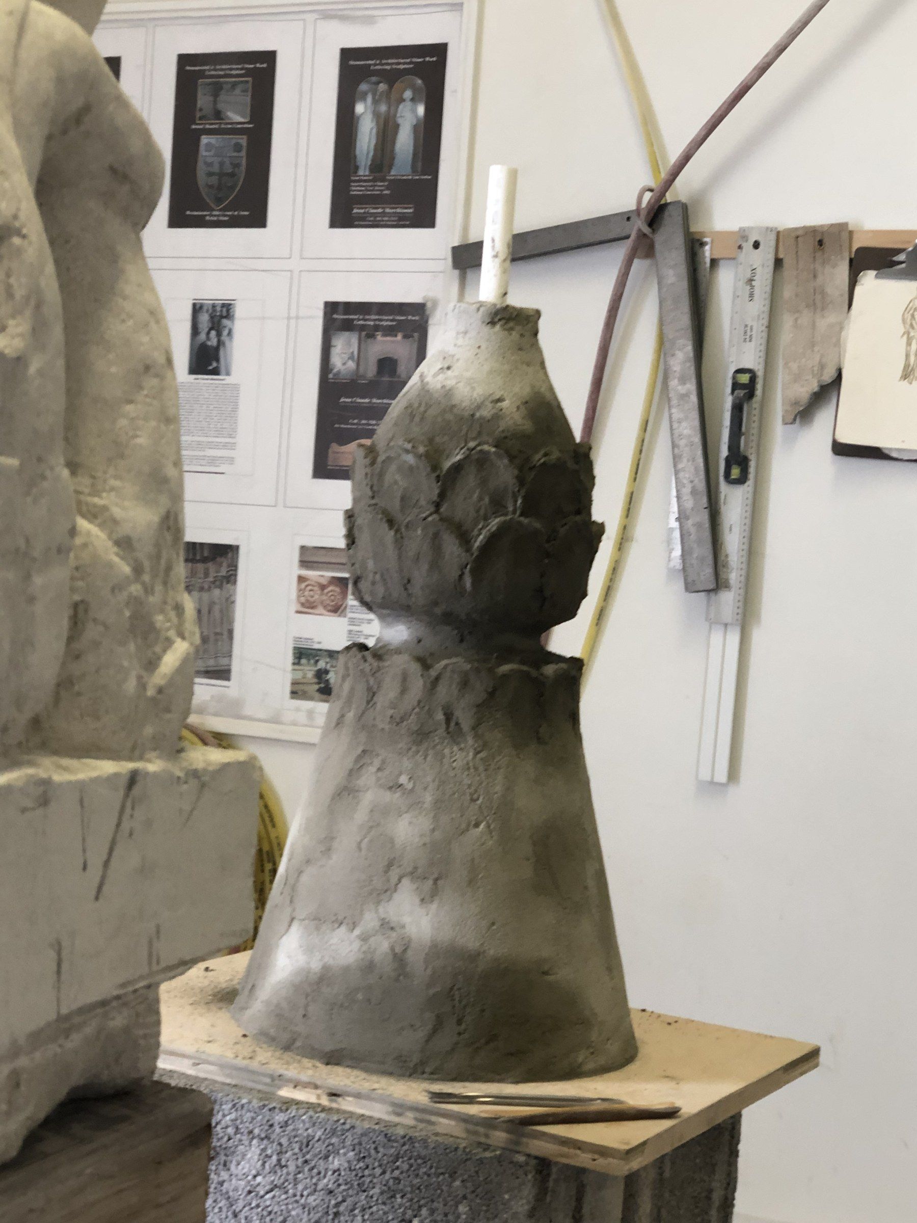 The finial in progress in the studio: a tapering cone wrapped in rows of overlapping leaves, on a wooden board.