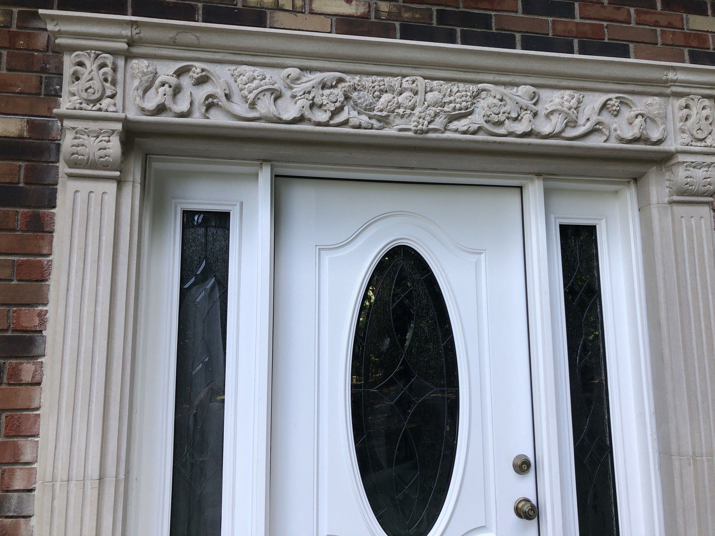 Vue rapprochée de la frise au-dessus de la porte : rinceaux, fleurs et fruits entre des blocs d'angle sculptés.