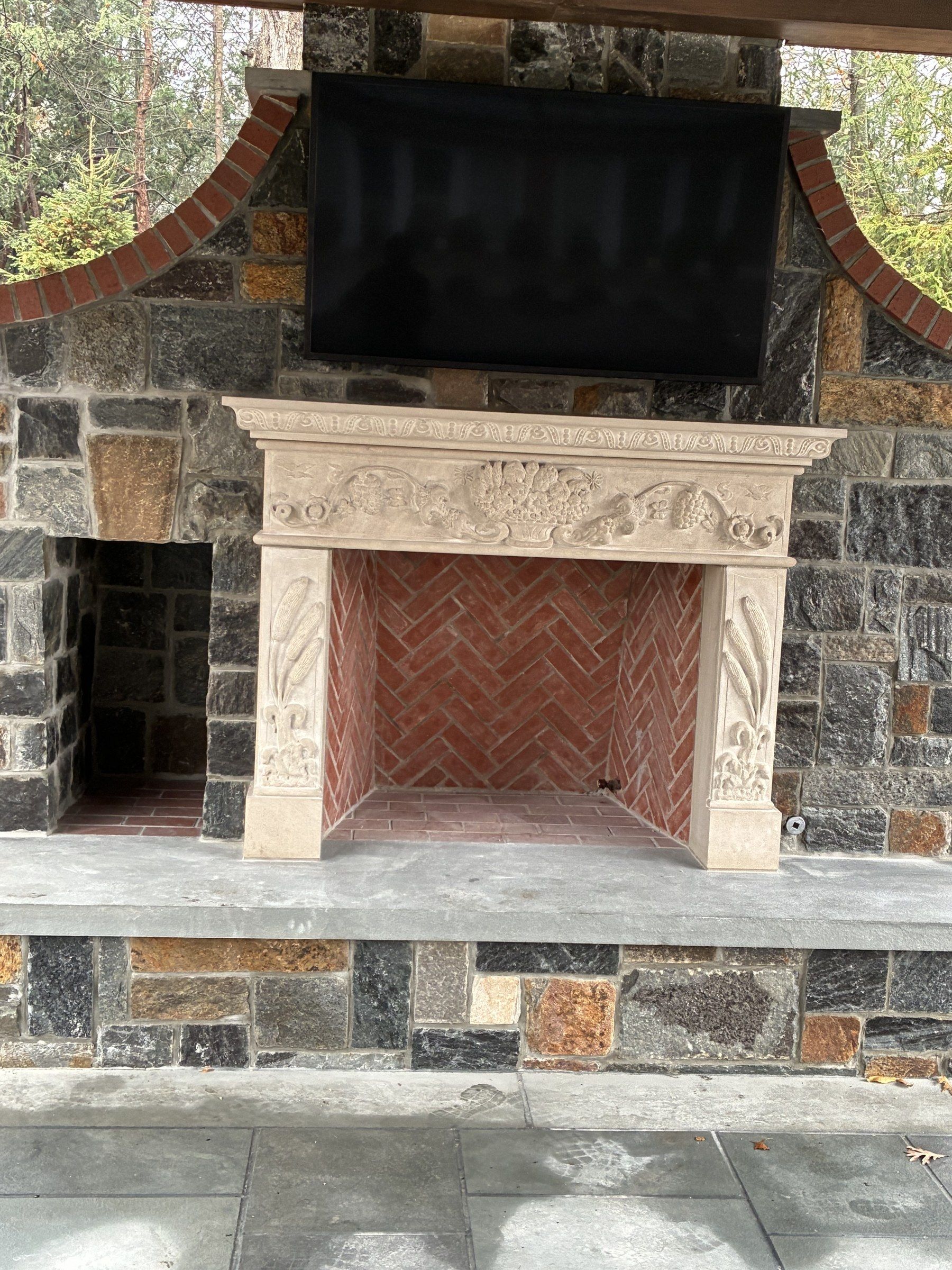 Front view of the outdoor fireplace, with the carved frieze and pilasters of the limestone mantel clearly visible.