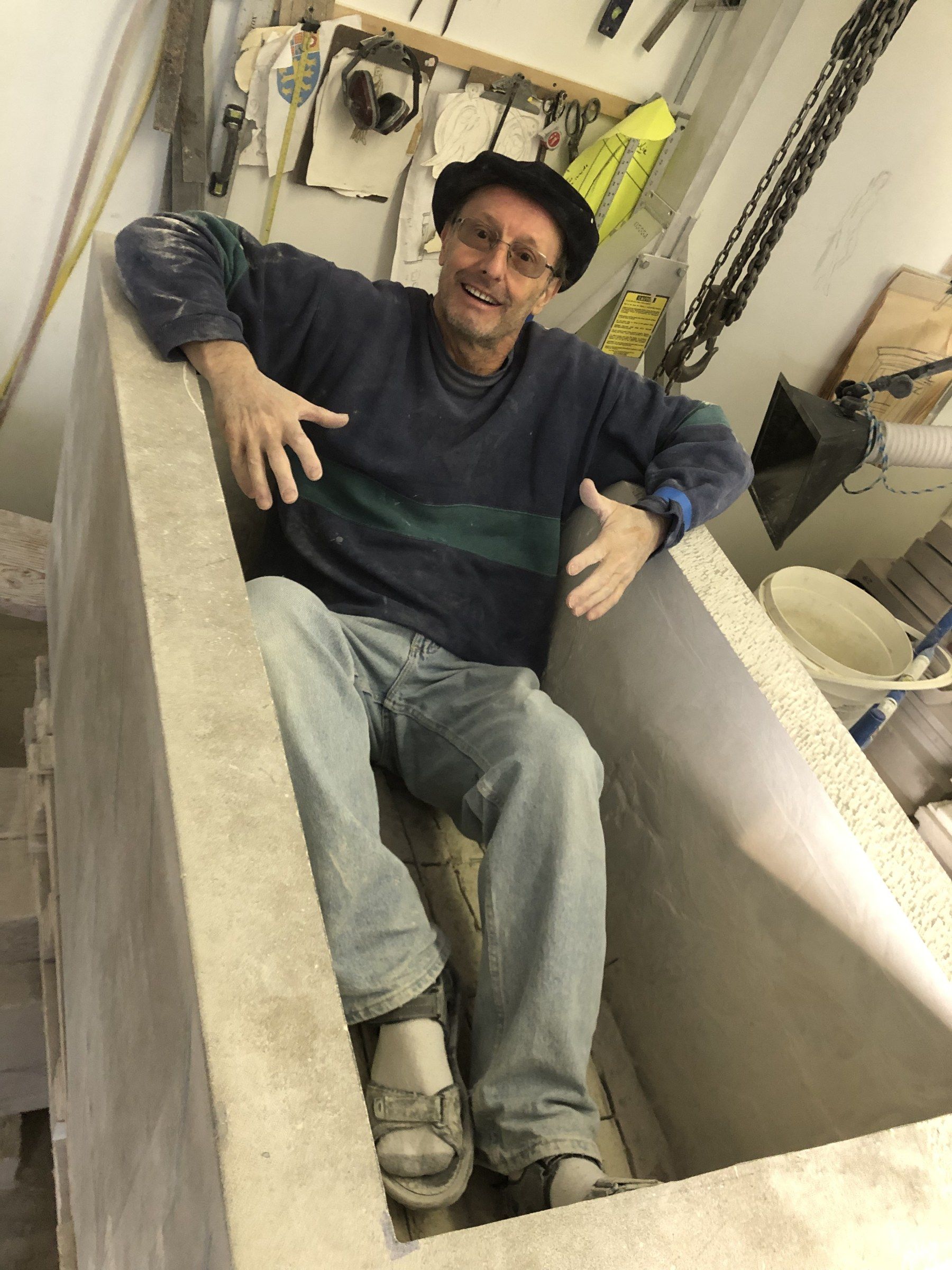 Jean-Claude Marchionni assis dans la jardinière creusée à l'atelier, souriant, les bras ouverts.