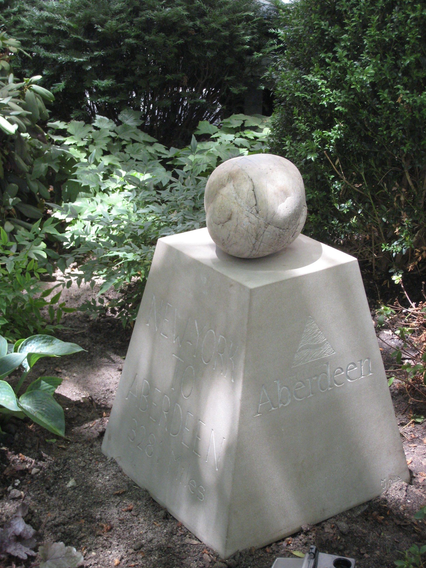 La borne dans l'ombre tachetée du jardin, ses deux faces sculptées visibles.