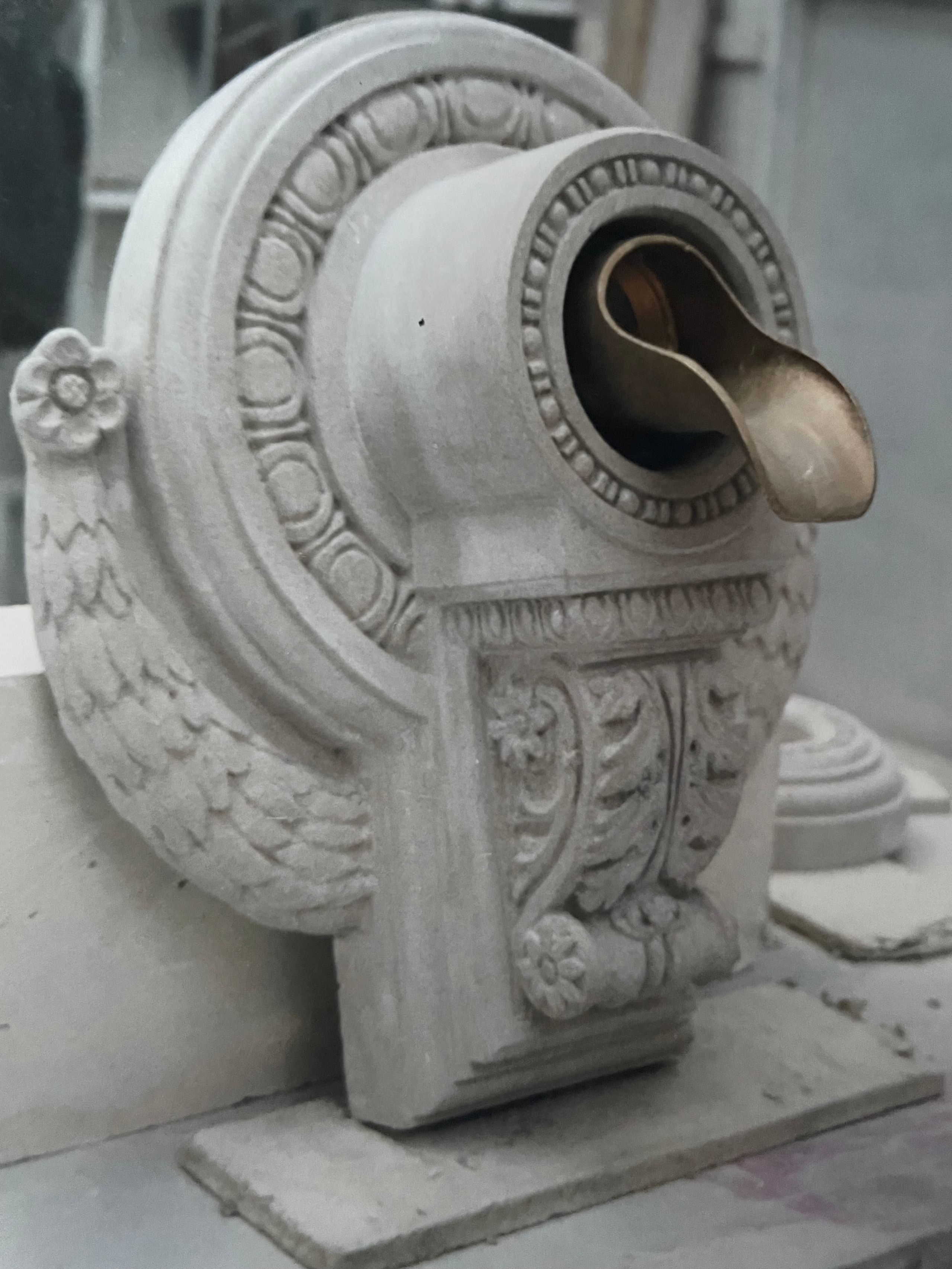 Ornate carved stone console with acanthus-leaf scrolls and an egg-and-dart border, fitted with a curved bronze drain spout.
