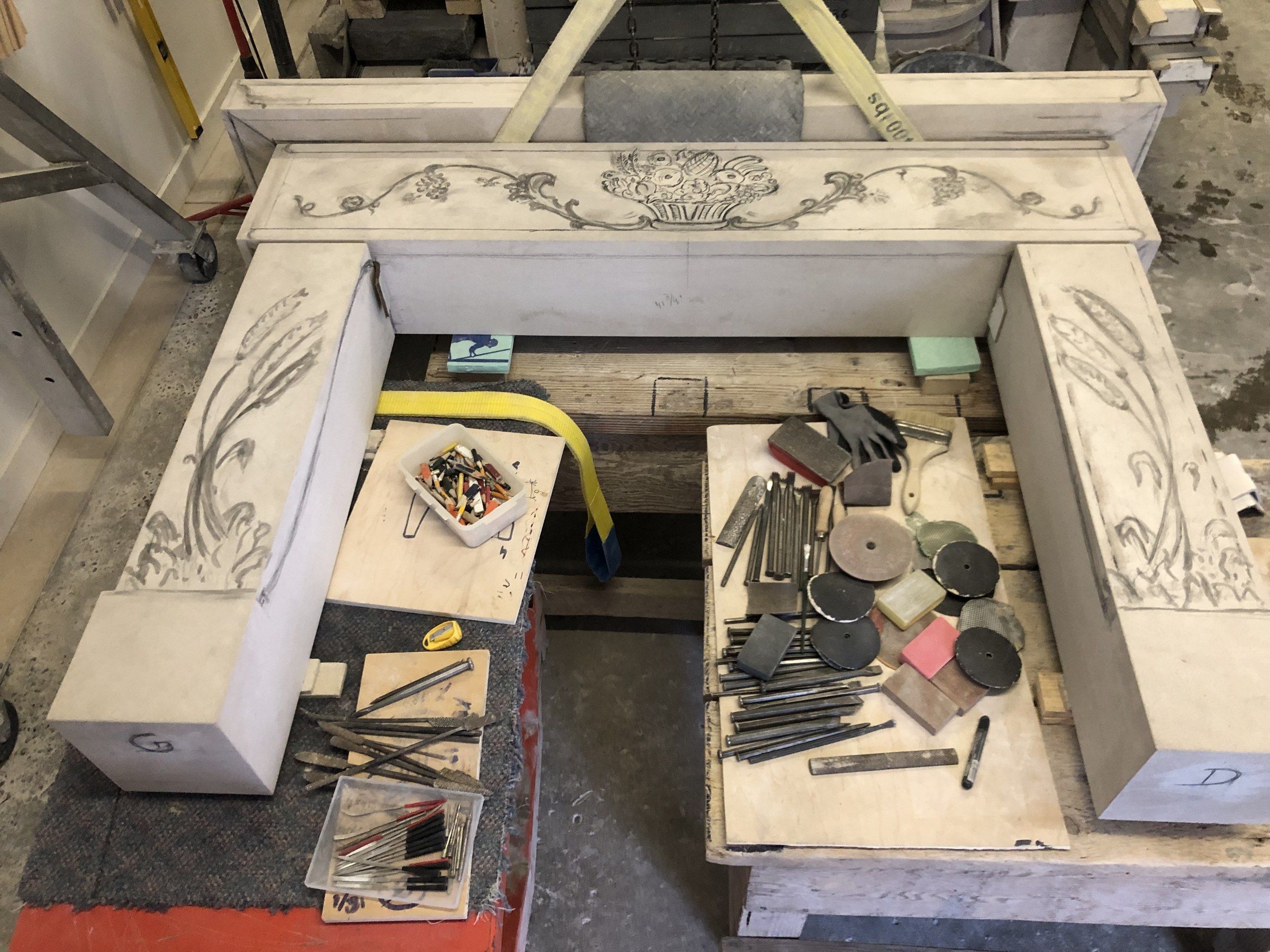 April 2025: the mantel's frieze and two jambs laid out on the bench, the fruit basket and scrolls drawn on the frieze and the ears of grain begun on the jambs.
