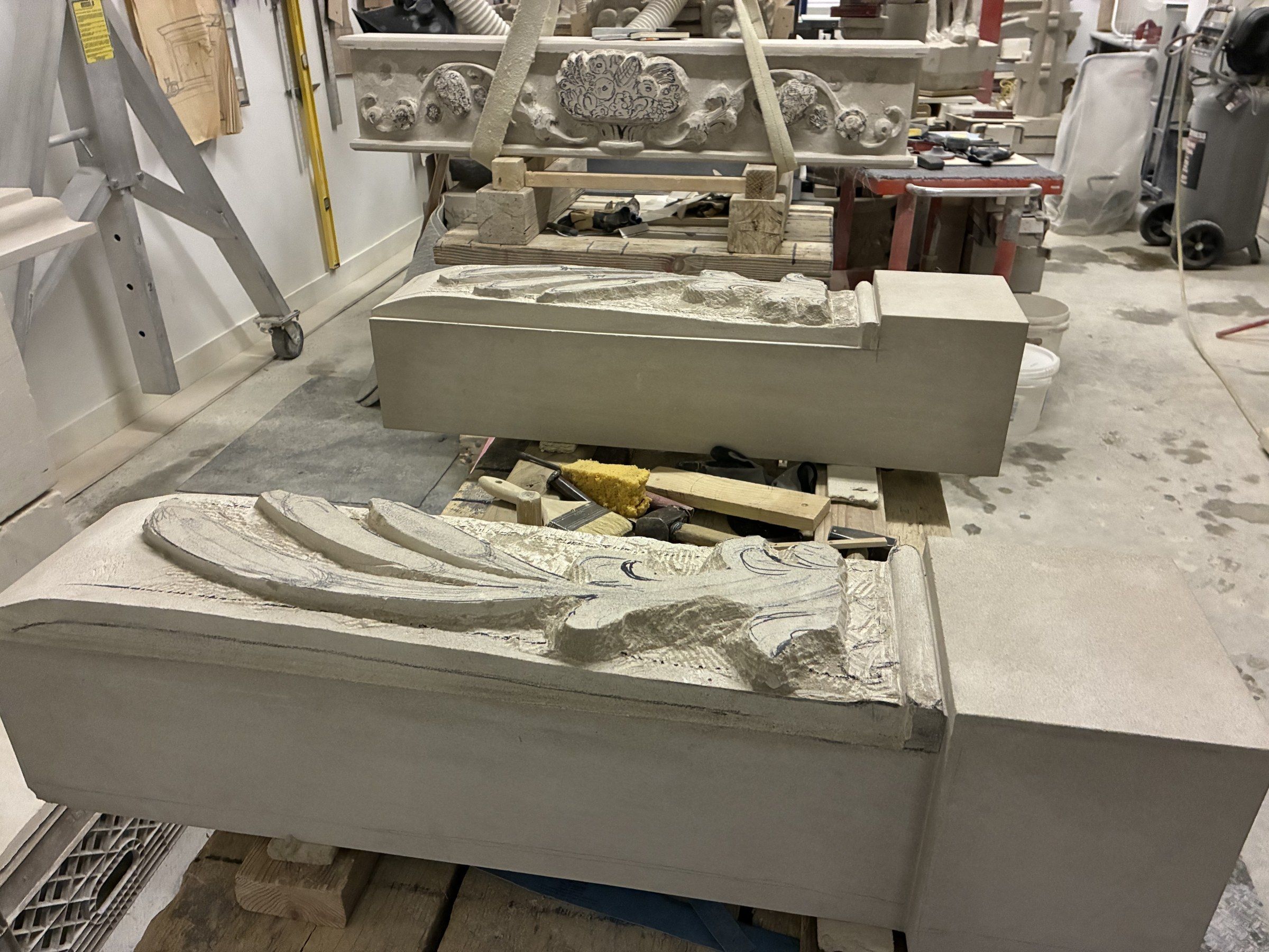 June 2025: a jamb carved with long ears of grain in relief, the carved frieze on its trestles behind it.