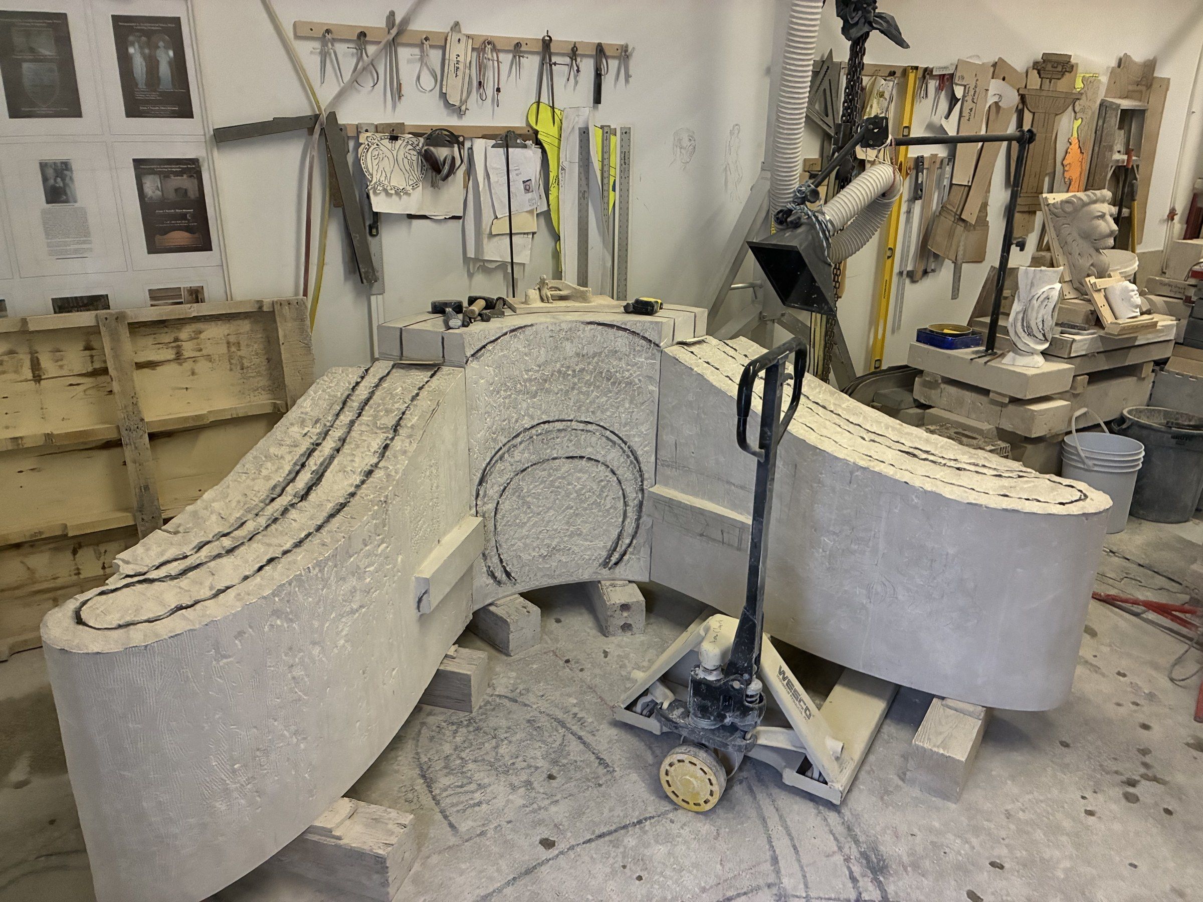 Two of the monument's curved wings carved separately, on rolling carts in the studio in April 2026 — a reminder that the final piece is an assembly of multiple blocks, not a single monolith.