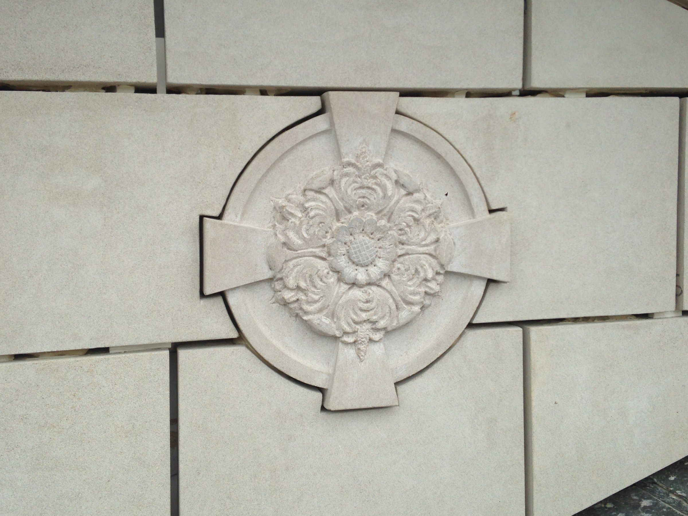 A finished rosette set among smooth stone panels, its flower surrounded by curling leaves.