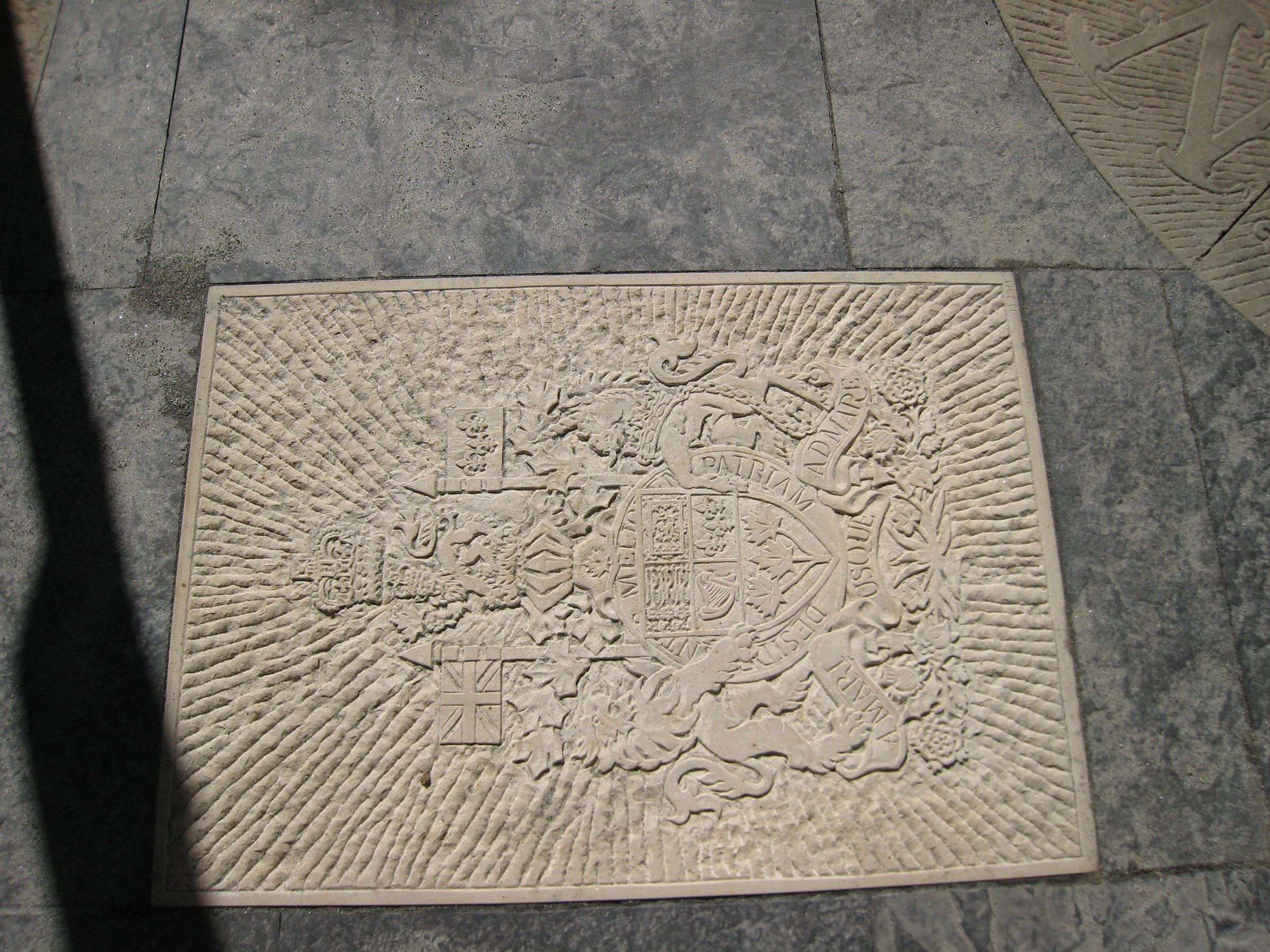 Le relief encastré dans le dallage de pierre du jardin, mi-soleil mi-ombre, au bord d'une autre pierre sculptée.