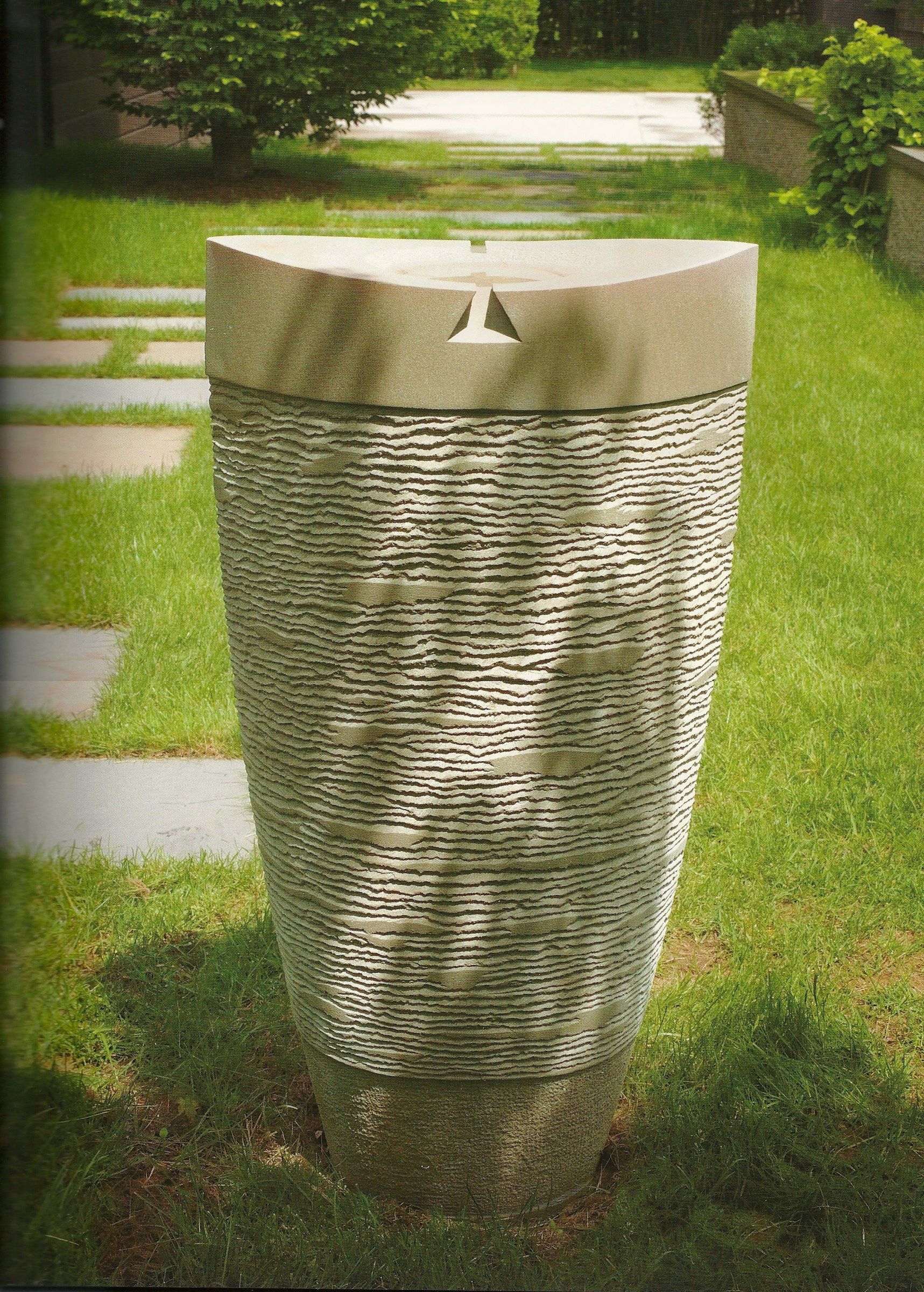 The stele seen close up on the lawn: its body carved in wavy horizontal ridges, a smooth top band with a small cut-out at the rim.