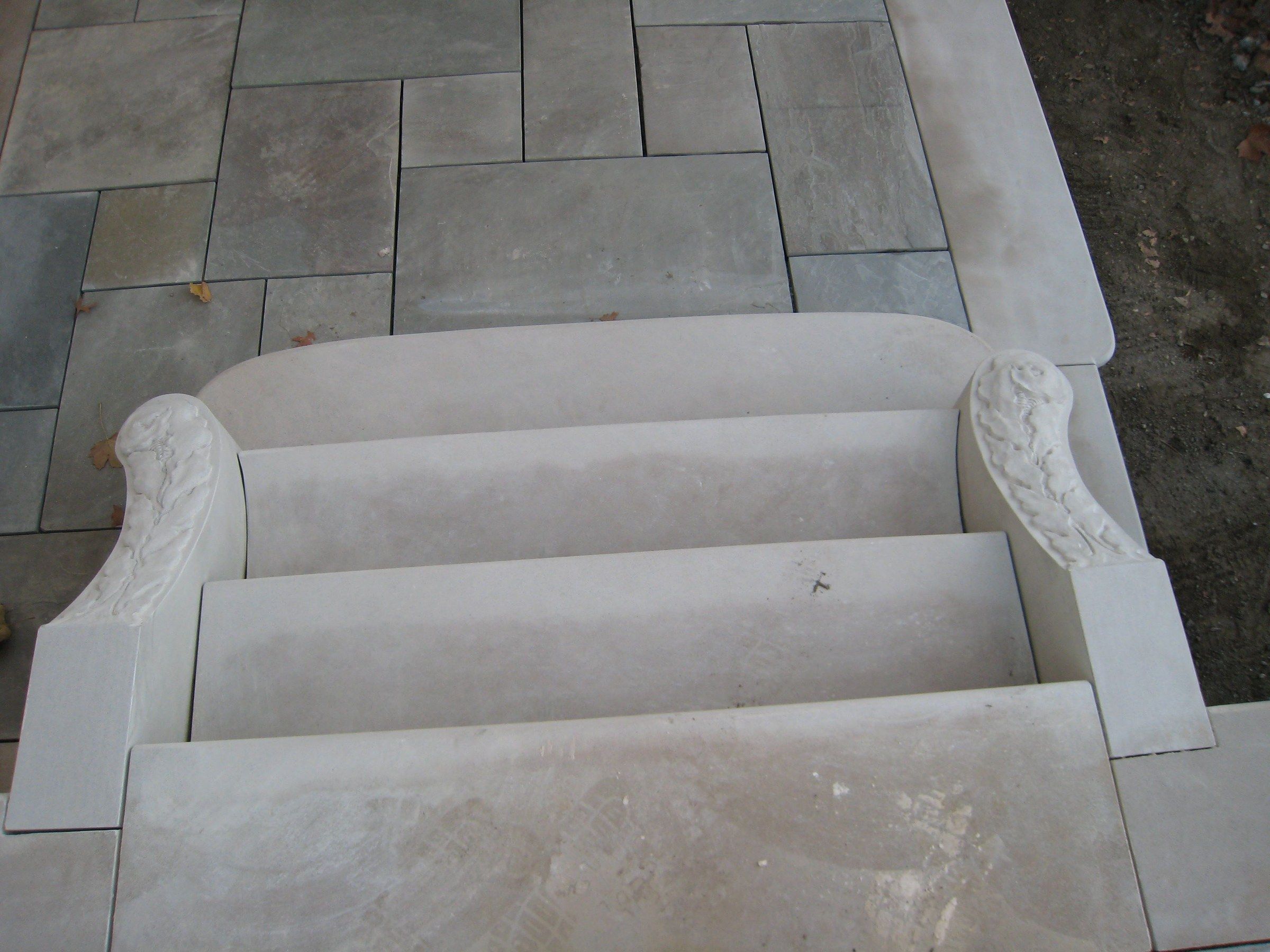 The steps seen from above, between the two carved volutes, with stone paving beyond.