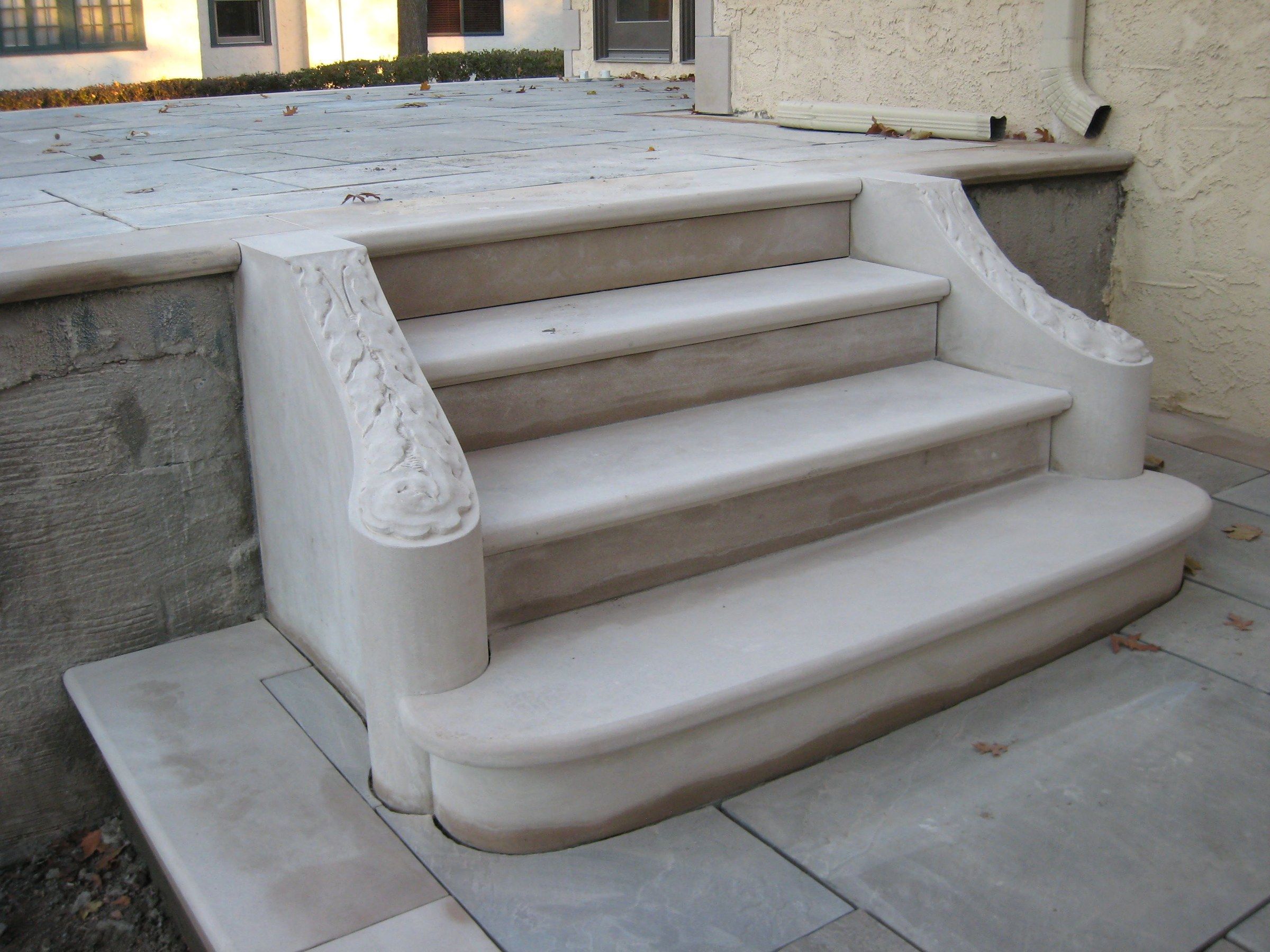 Limestone entrance steps seen from the side: rounded treads between two side walls, each ending in a scroll carved with leaves.