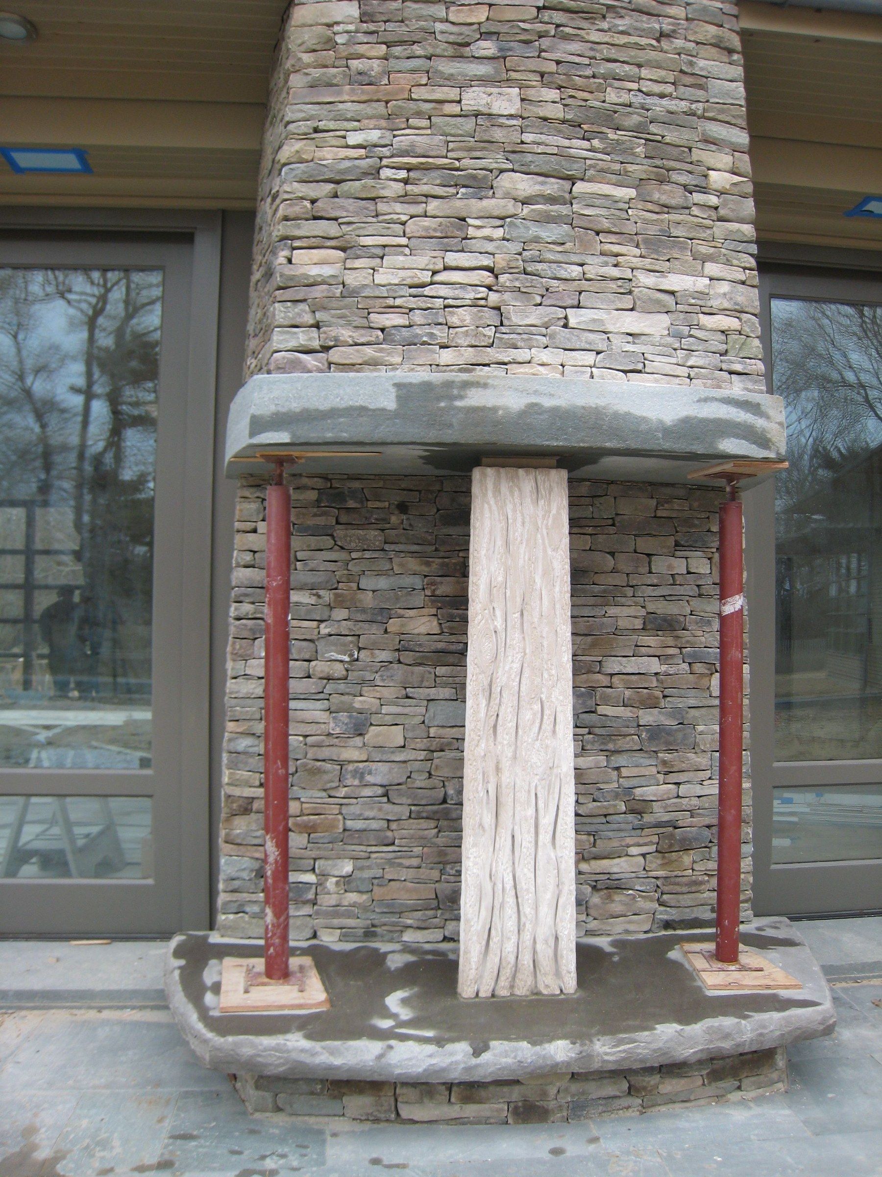 The trunk column during installation, set between walls of stacked stone beneath a heavy stone mantel held on temporary red supports.