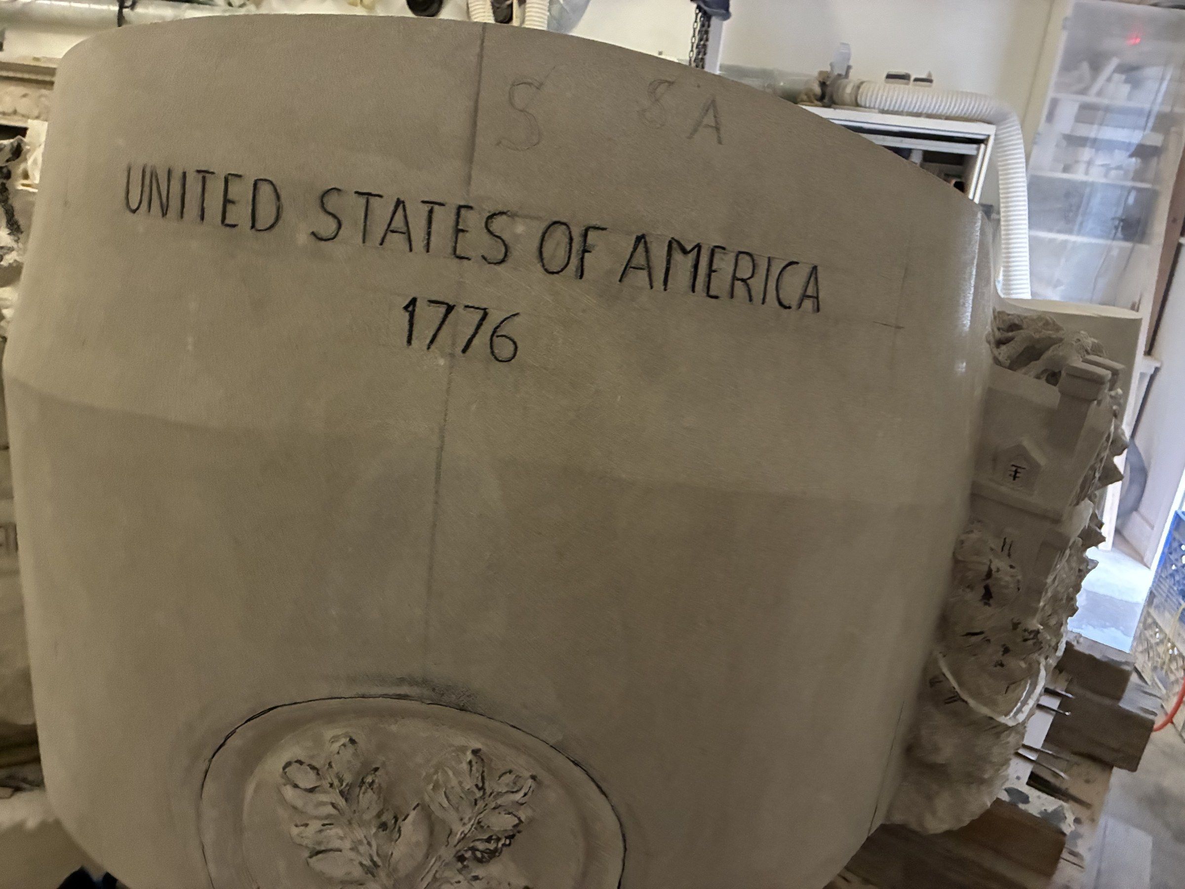 The inscription “UNITED STATES OF AMERICA 1776” carved across a curved panel in August 2026, above the oak-leaf medallion.