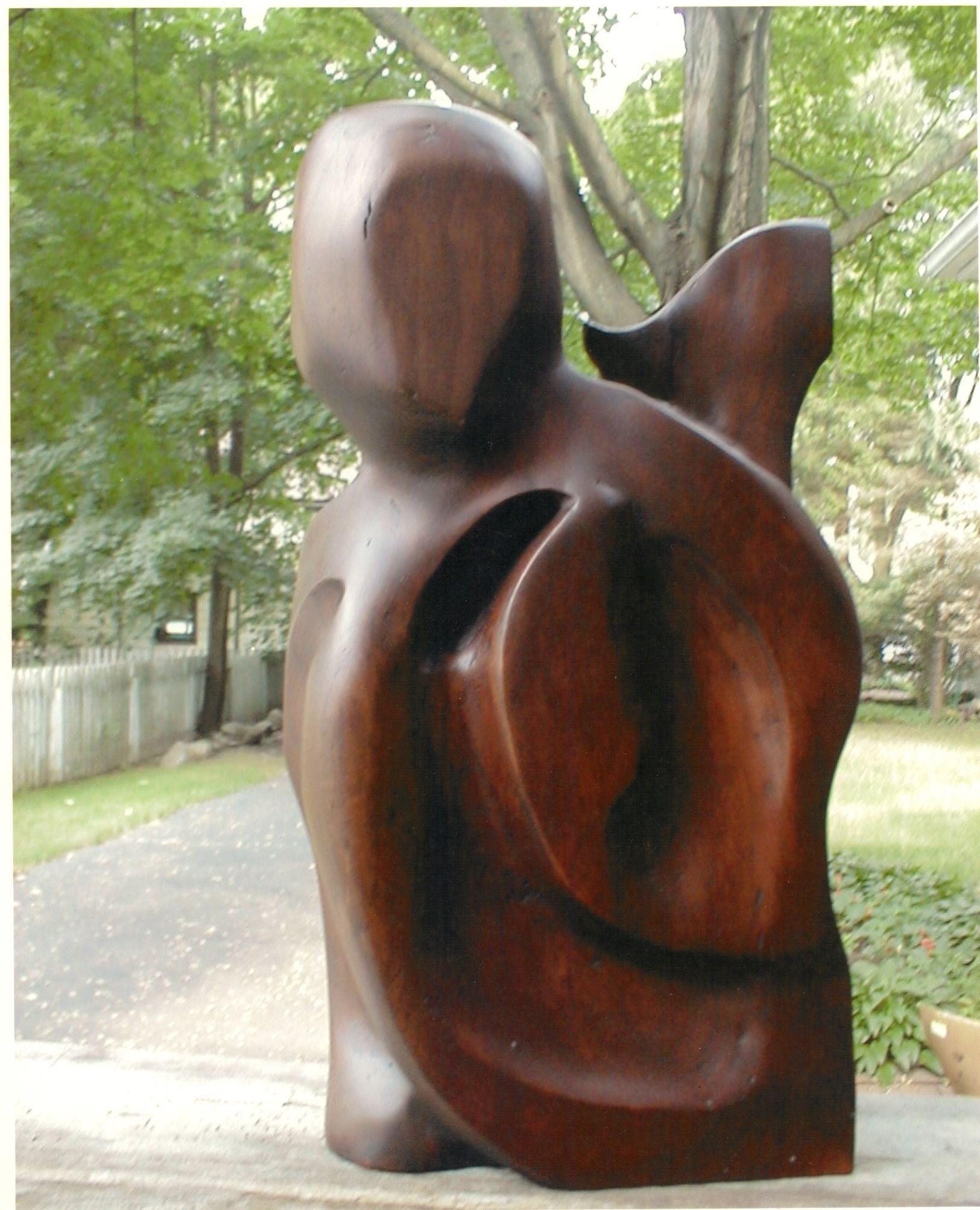 The other side of the sculpture: a smooth, rounded head-like form at the left, and a broad curving band that wraps around a smaller enclosed form, read as an arm holding a child.