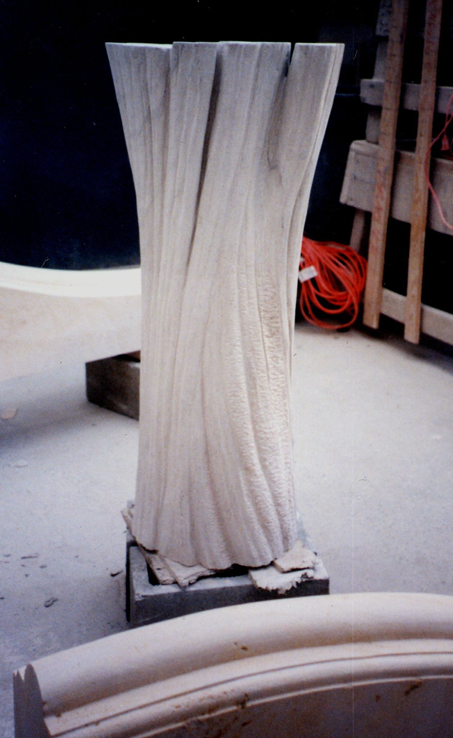 The carved stone trunk photographed in the workshop before installation, showing deep vertical fluting that reads as bark across the full height of the column.